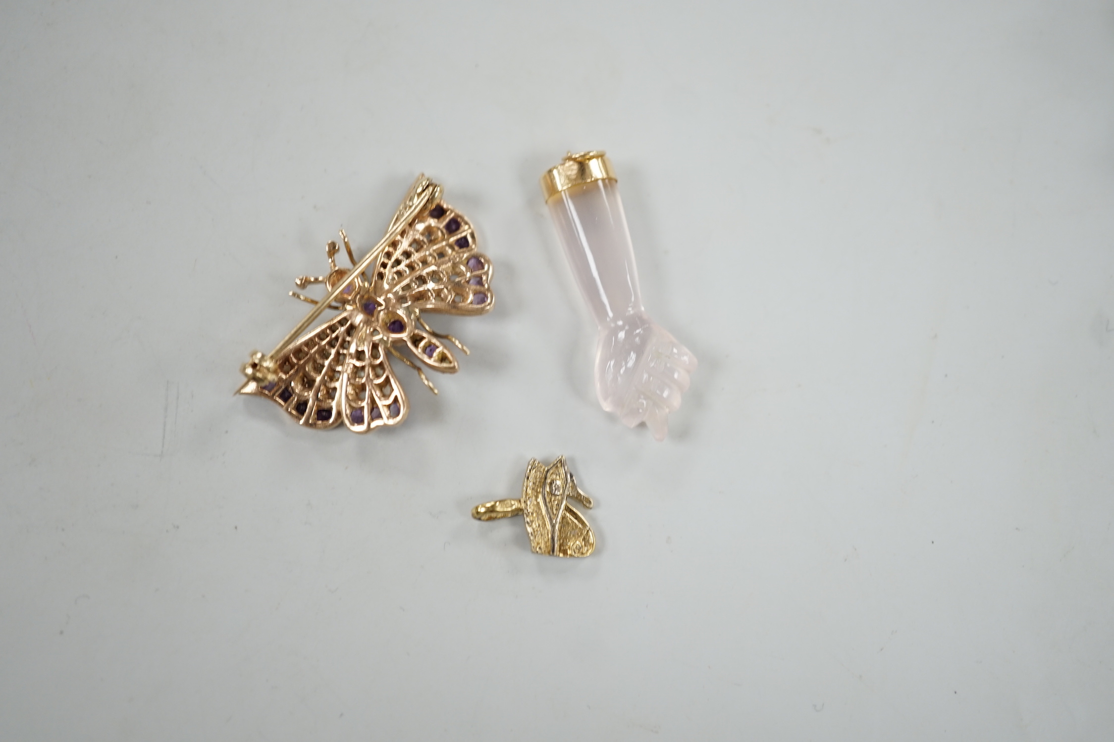 A modern 9ct gold, amethyst and seed pearl cluster set butterfly brooch, width 32mm, together with two charms including arm and fist.